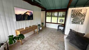 Una sala de estar con un televisor grande, un banco de madera, un sofá y vistas a un campo verde a través de grandes ventanales.