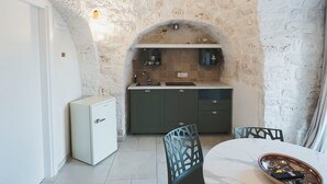 Un interno con soffitto in pietra, angolo cottura con lavello e pensili, e tavolo da pranzo con sedie.