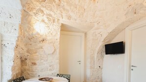 Una stanza dalle pareti in pietra con un tavolo rotondo e sedie, una TV a schermo piatto montata a parete e una porta vetrata che dà sull'esterno.