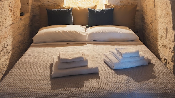 Una stanza con pareti in pietra, un letto, dei cuscini e una finestra.