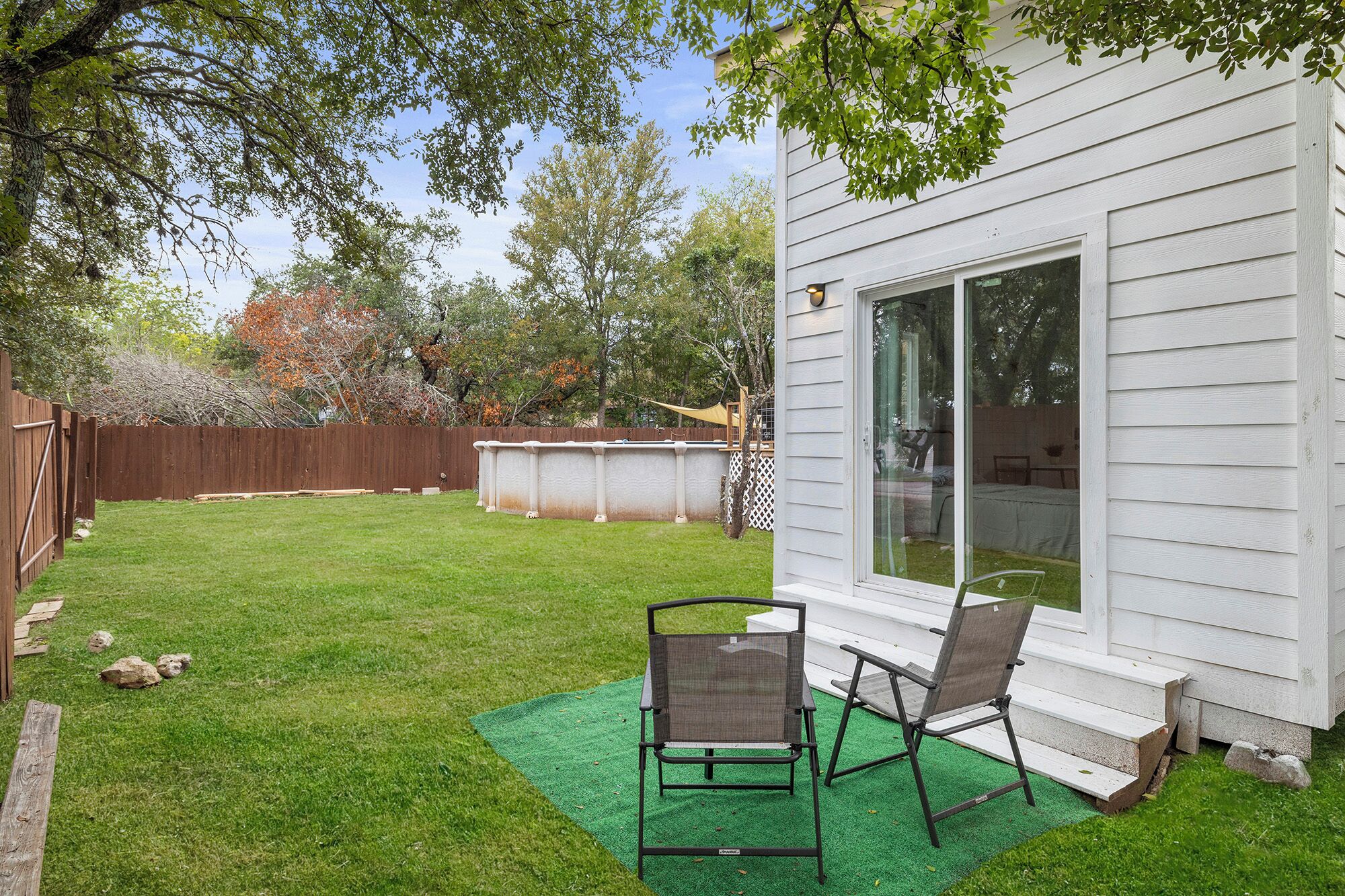 A backyard with a lawn, two chairs, a wooden fence, and a house with a sliding glass door.
