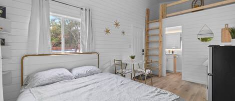 Un dormitorio con cama, una pequeña mesa con sillas, una escalera y vistas al baño.