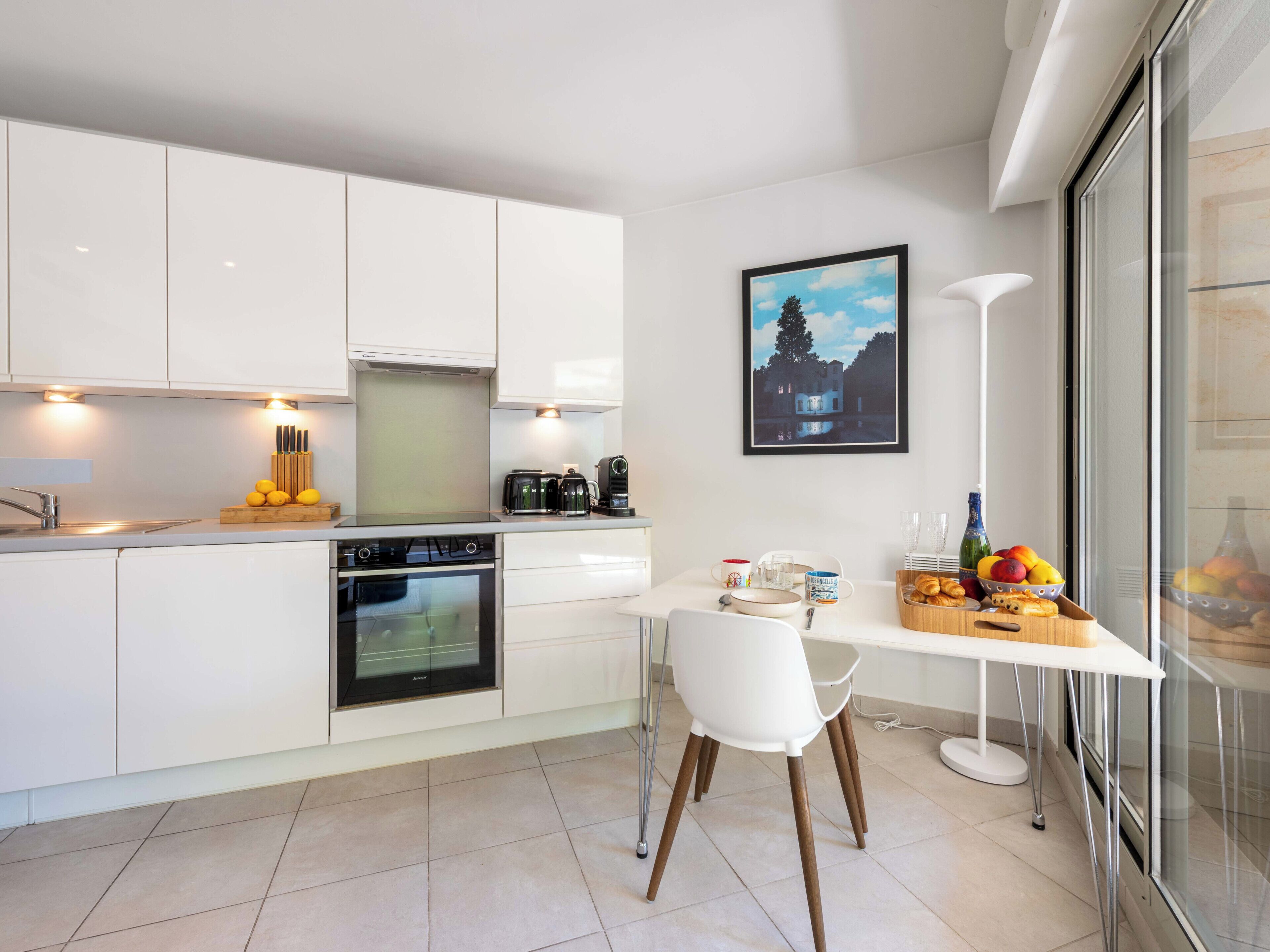 Una cocina moderna con armarios blancos, horno empotrado y comedor con mesa y silla blancos.