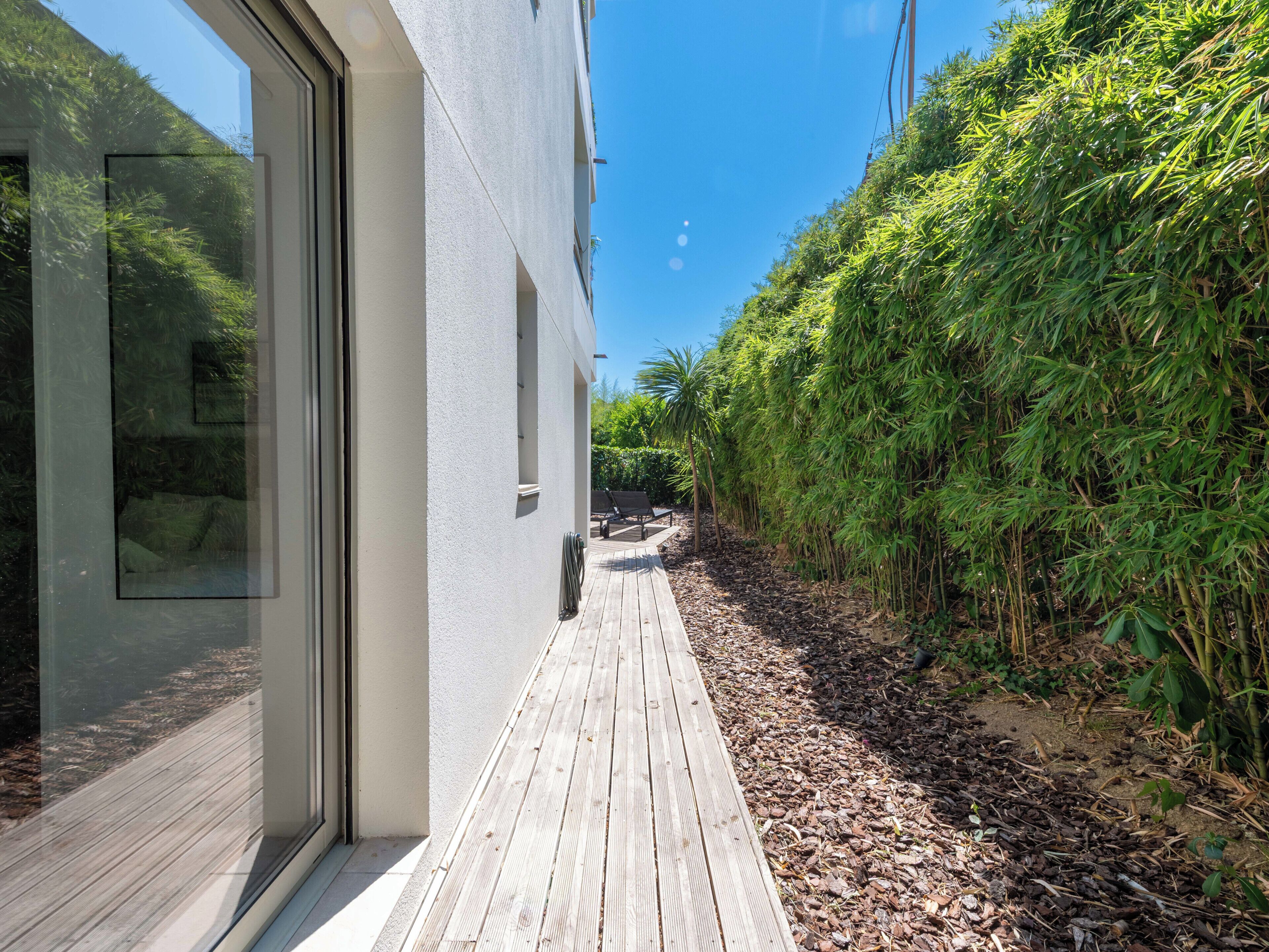 Un edificio moderno con terraza de madera, puertas de cristal y jardín de bambú.