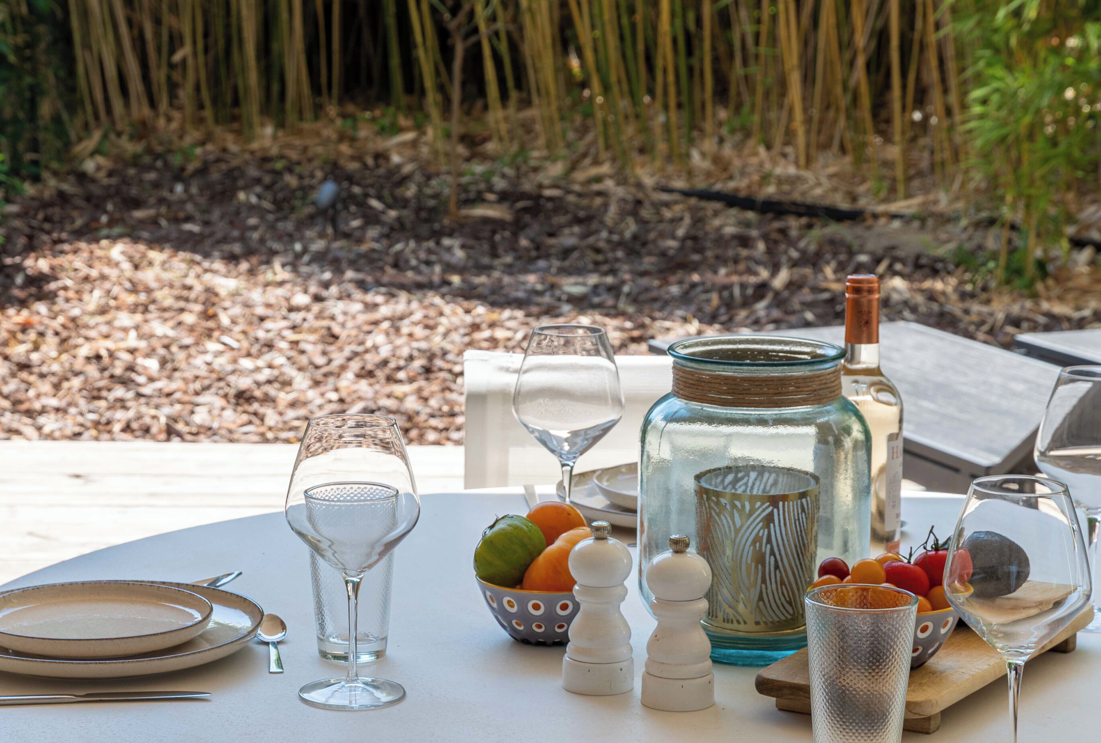 Mesa al aire libre con una botella, saleros y pimenteros, un bol de fruta y copas de vino.