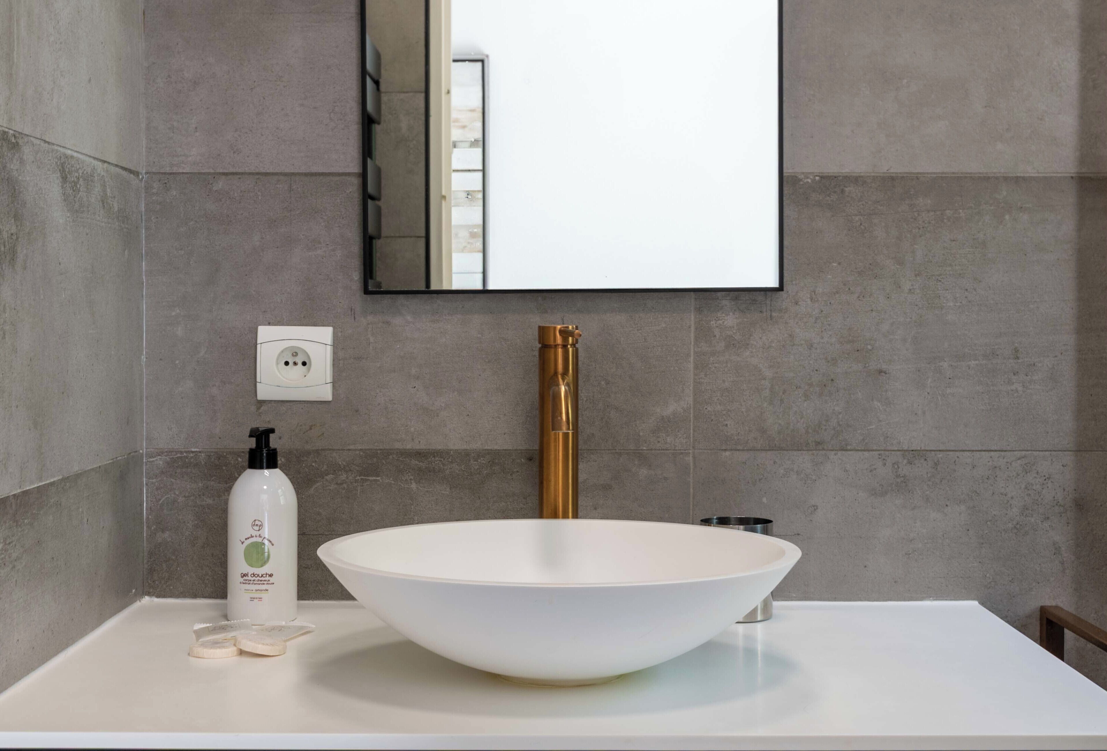 A bathroom with a white sink, a gold faucet, and a bottle of soap on the counter.