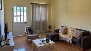 Ein Wohnzimmer mit einer Couch, einem Sessel, einem Couchtisch und einem Fernseher auf einem Schrank.