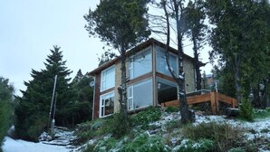 Una casa moderna de dos pisos con ventanas amplias, rodeada de árboles y un paisaje nevado.