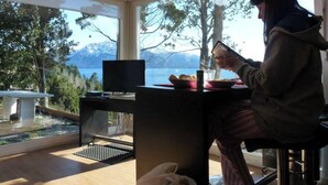 Una persona sentada a una mesa con un ordenador portátil y un vaso de agua, con vistas a un paisaje de un lago y montañas.