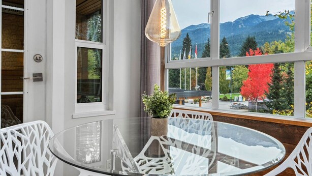 A modern room with a glass table and chairs, a hanging light fixture, and a large window with a mountain view.
