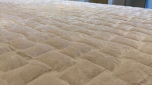 Een bed met een gewatteerde spreidekbed in een kamer met een deur naar een gang.