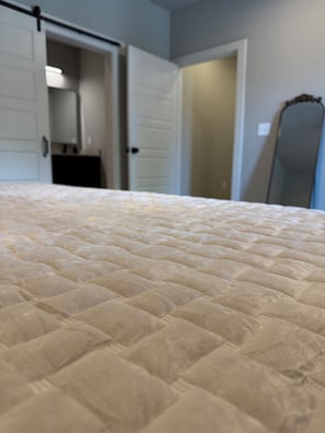 Un letto con copriletto trapuntato in una stanza con una porta che dà su un corridoio.