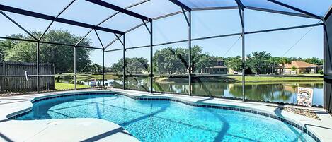 A swimming pool with a clear view of the surrounding area, including a wooden fence and a body of water.