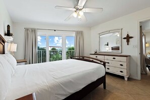 Een slaapkamer met een groot bed, een dressoir, een plafondventilator en een balkon met gordijnen.