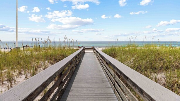 Une promenade en bois qui mène à une plage, avec un ciel dégagé et une vue imprenable sur l’océan.