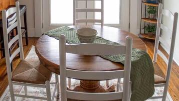 Un espace repas avec une table ronde en bois, des chaises blanches et un chemin de table vert.