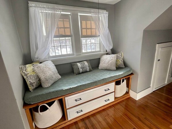 A cozy room with a built-in bench, a window with sheer curtains, and a door.