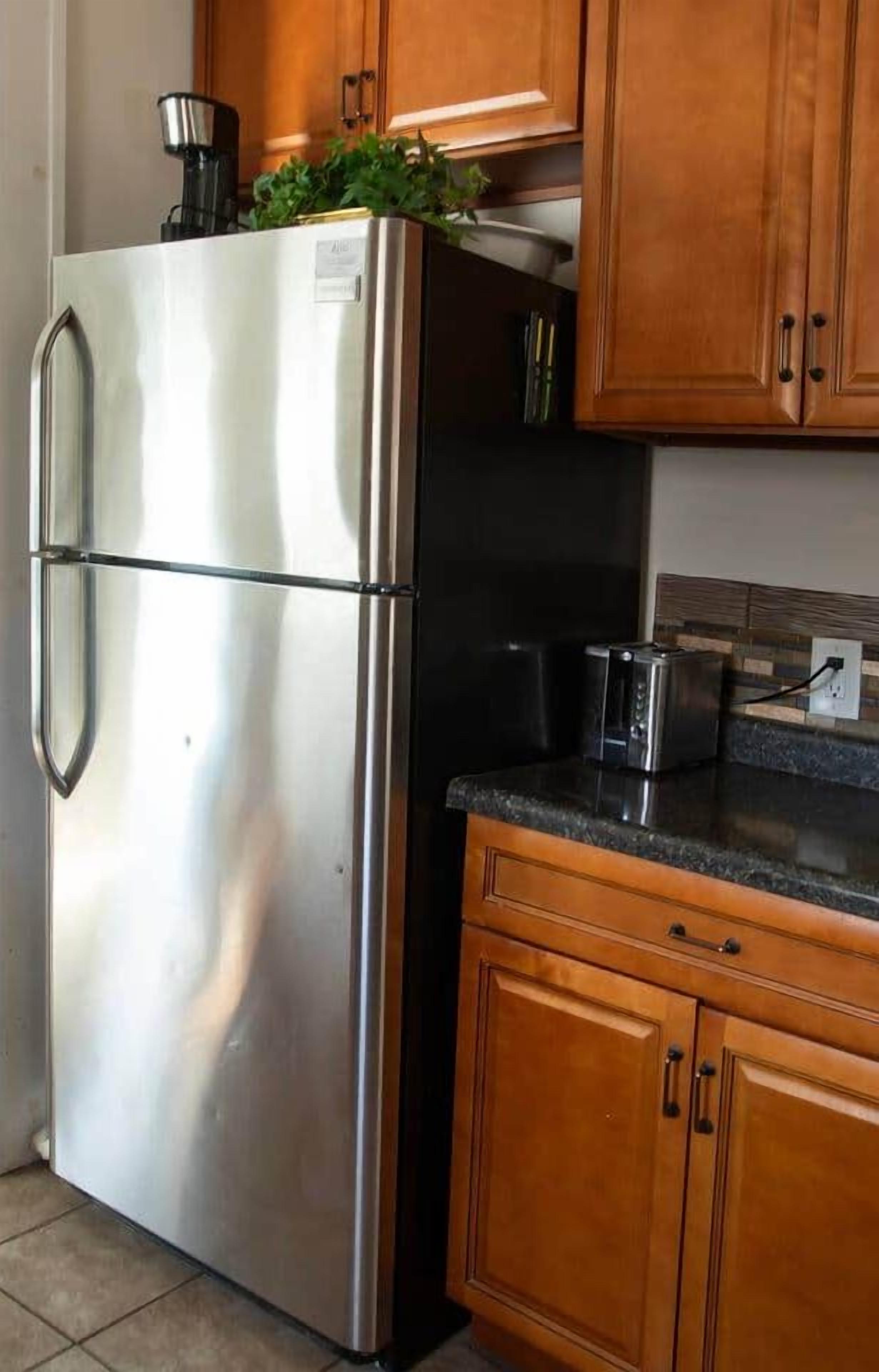 A stainless steel refrigerator with a coffee maker on top, wooden cabinets, a toaster, and a tiled backsplash.