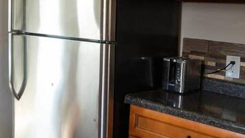 A stainless steel refrigerator with a coffee maker on top, wooden cabinets, a toaster, and a tiled backsplash.