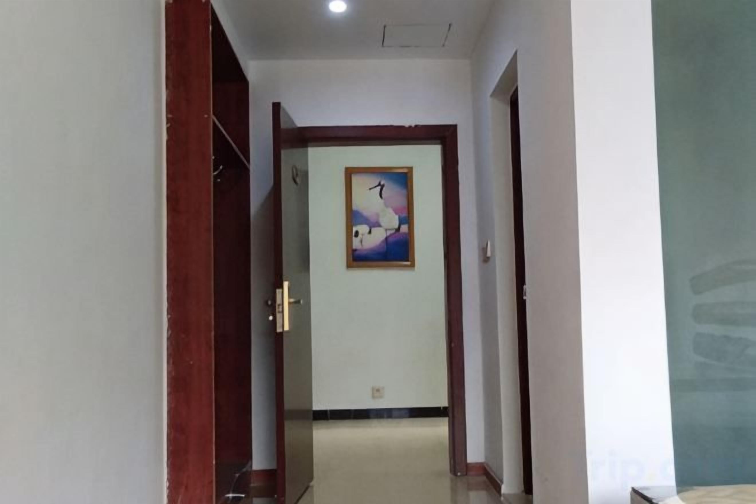 Un pasillo con una puerta de madera, un cuadro en la pared y un suelo de baldosas.
