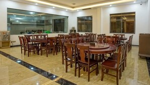 Un comedor con varias mesas redondas y sillas, ventanas amplias y una cocina al fondo.