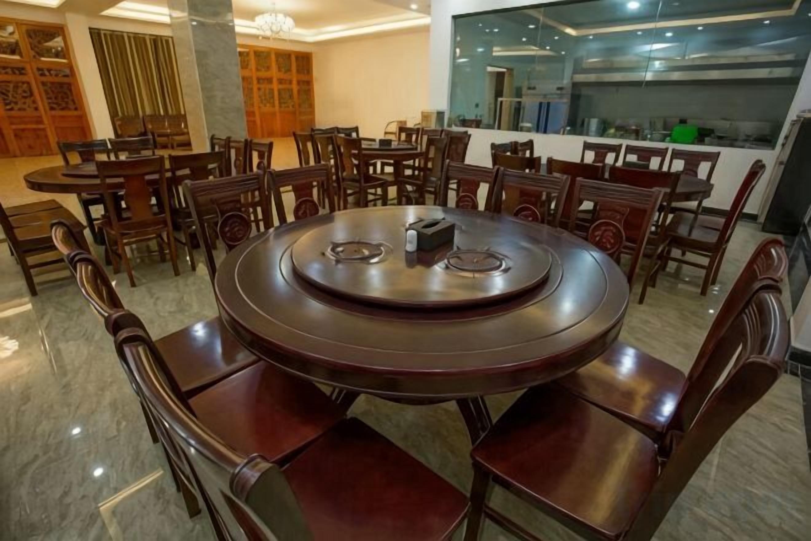 A round dining table with chairs, a chandelier, and a kitchen area in the background.