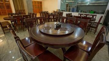 A round dining table with chairs, a chandelier, and a kitchen area in the background.