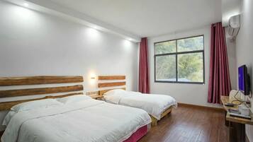 A room with two beds, a desk, a computer, and a window with curtains.