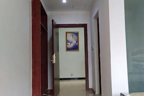 A hallway with a wooden door, a framed picture on the wall, and a tiled floor.