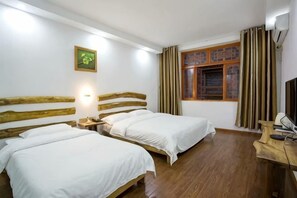 A room with two beds, wooden headboards, a desk, a chair, a window with curtains, and a wall-mounted light.