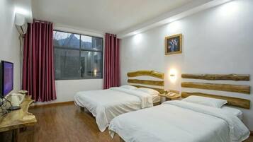Habitación de hotel con dos camas, un escritorio con computadora, una ventana con cortinas y una lámpara fijada a la pared.
