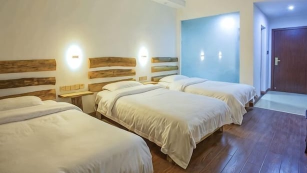 Habitación de hotel con tres camas, cabeceros de madera, lámparas de noche y una pared azul decorativa.