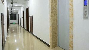 Un pasillo largo y estrecho con puertas a ambos lados, una pared de mármol y un panel de control digital de ascensor.