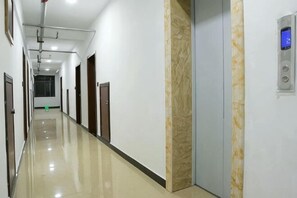 A long, narrow hallway with doors on both sides, a marble wall, and a digital elevator control panel. - Fenglinge Hotel (Zhangjiajie)