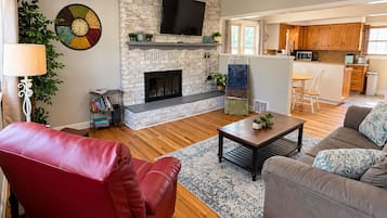 A living room with a fireplace, a television, and a dining area with a kitchen in the background.