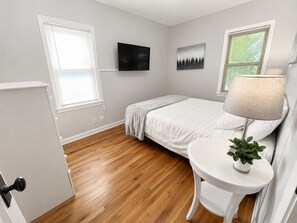 A bedroom with a bed, a TV, a lamp, and a window.