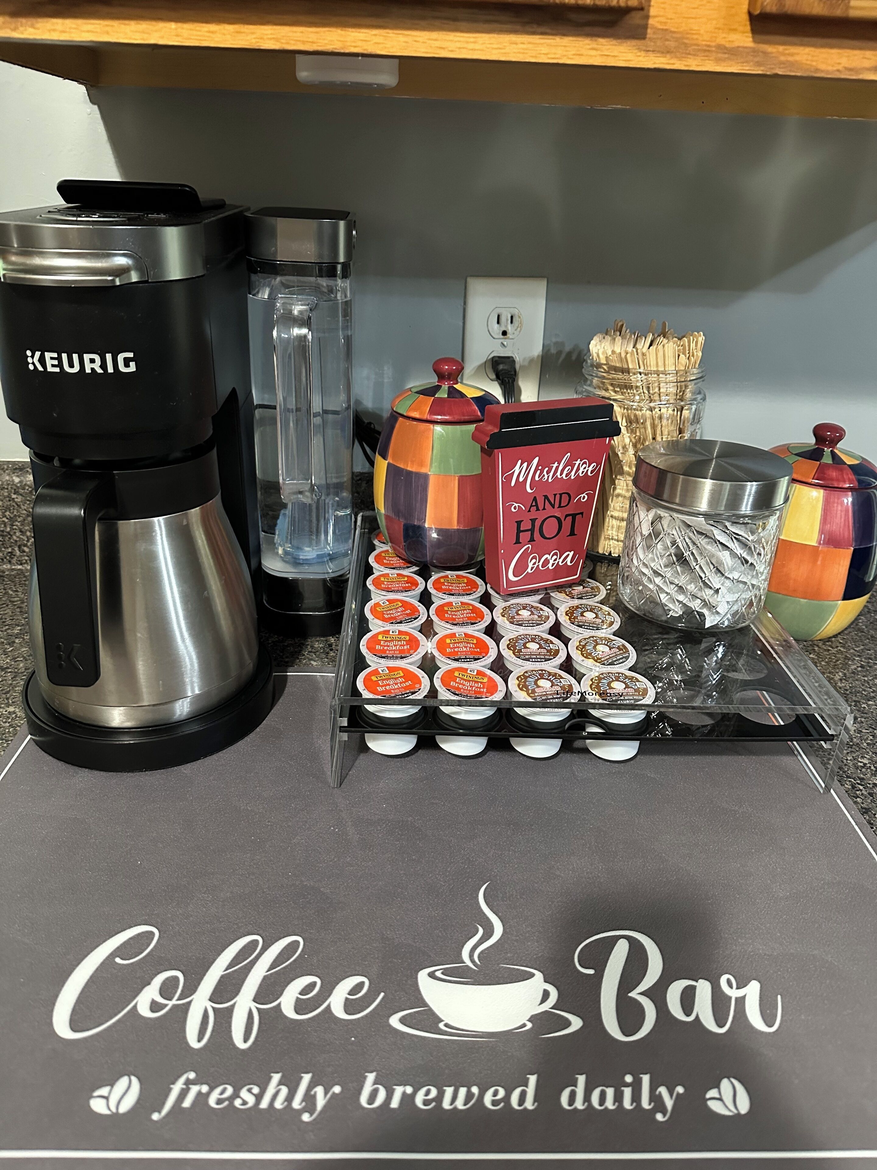 A coffee station with a Keurig coffee maker, a mug, a colorful teapot, and a tray of English breakfast pastries.