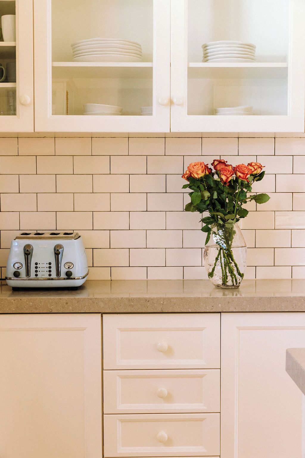 Een keuken met witte kastjes, een broodrooster op het aanrecht en een vaas met bloemen.