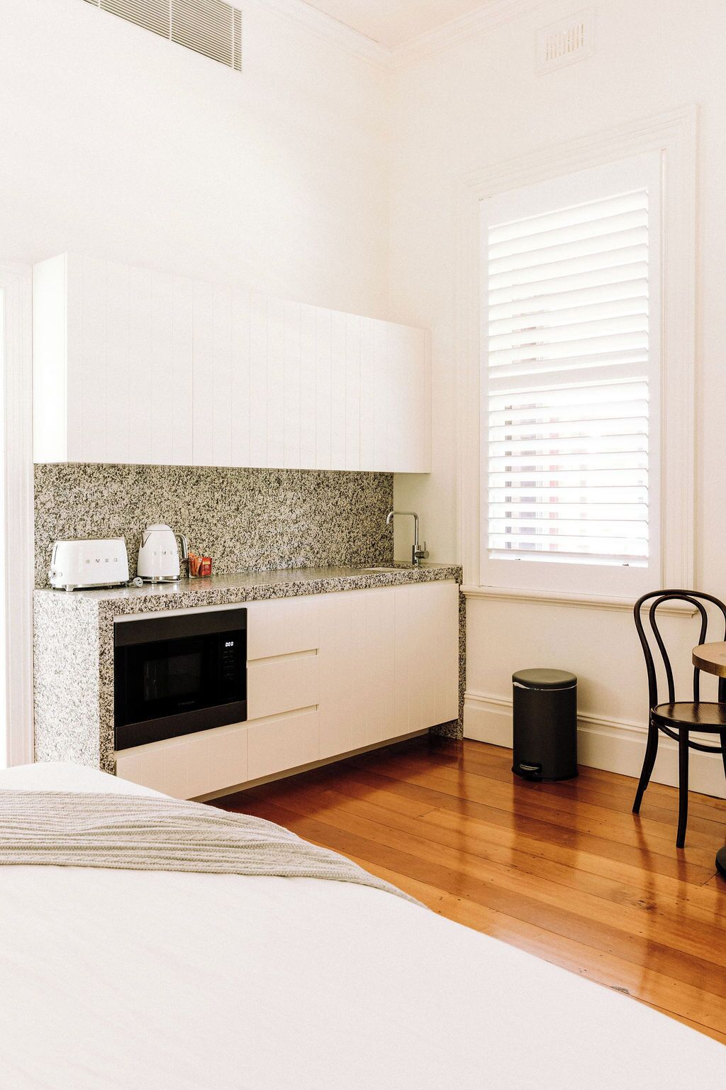A compact kitchen with white cabinets, a granite countertop, a built-in oven, and a window with blinds.