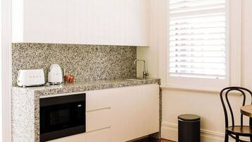 A compact kitchen with white cabinets, a granite countertop, a built-in oven, and a window with blinds.