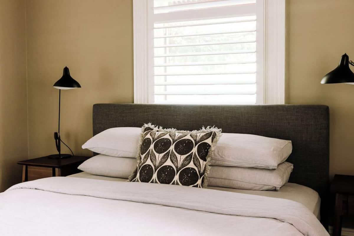 A neatly made bed with a grey headboard, a patterned pillow, and two bedside lamps.