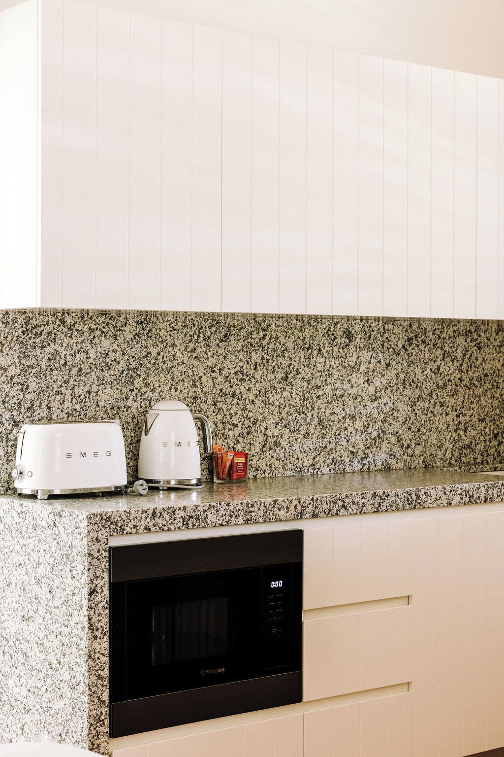 A kitchen with white cabinets, a granite countertop, a toaster, a kettle, and a microwave.