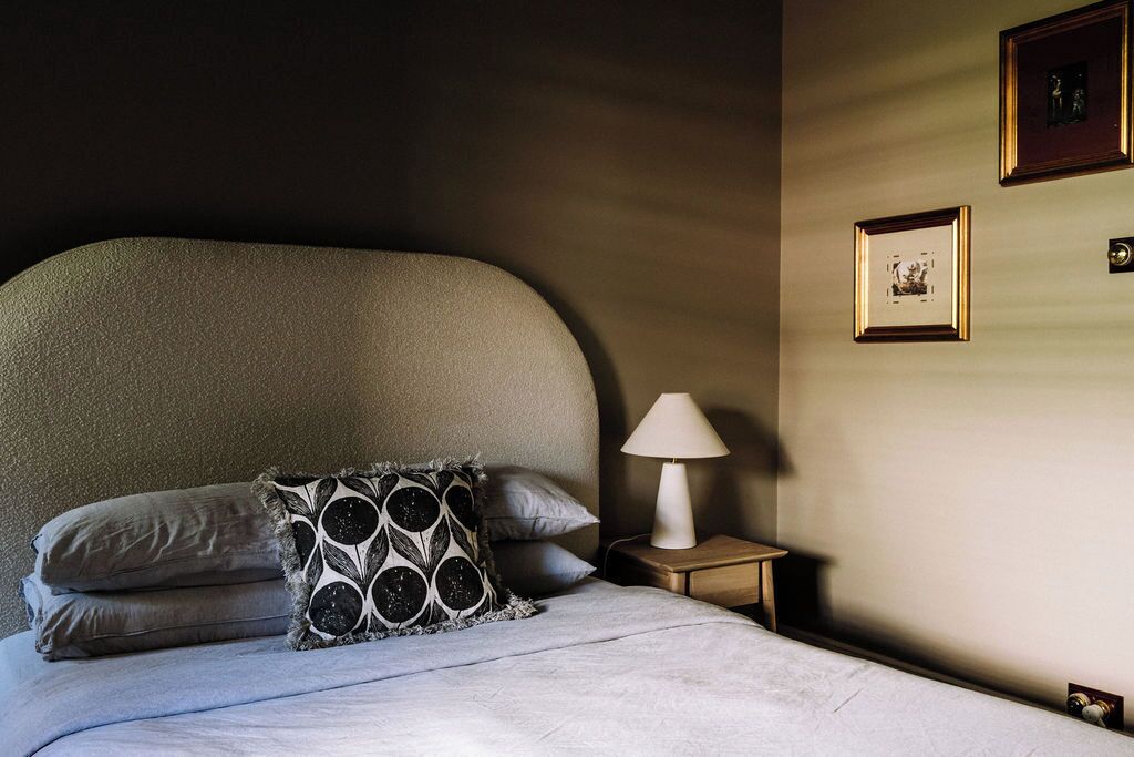 Cama bem arrumada com almofada estampada, luminária de cabeceira e quadros na parede.