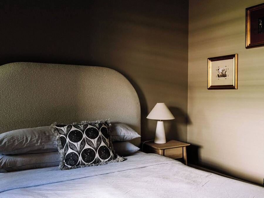 Cama bem arrumada com almofada estampada, luminária de cabeceira e quadros na parede.