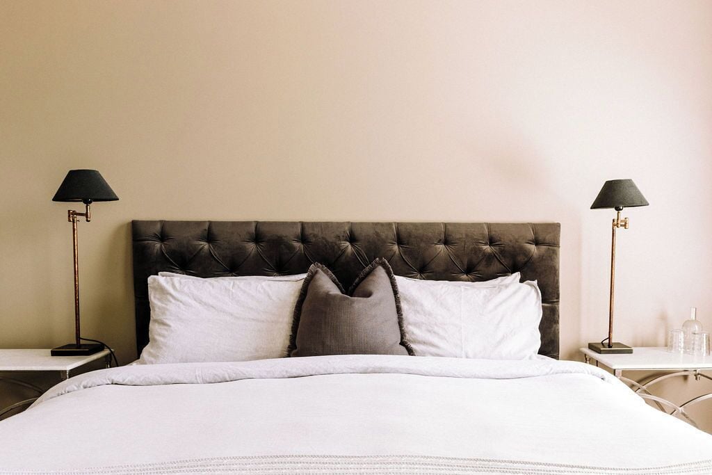 A neatly made bed with a tufted headboard, two bedside tables with lamps, and a plain wall.