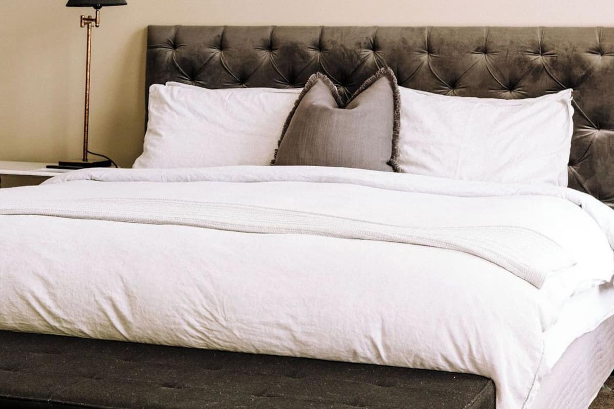 A neatly made bed with a tufted headboard, a bedside lamp, and a bench at the foot of the bed.