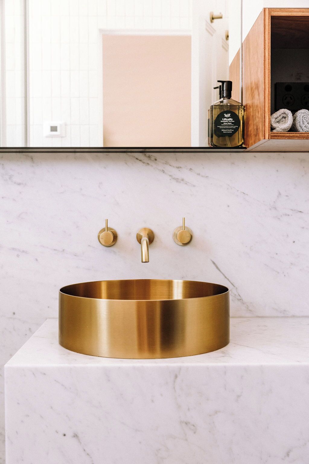 Een badkamer met een gouden wastafel, een marmeren aanrechtblad en een spiegel erboven.