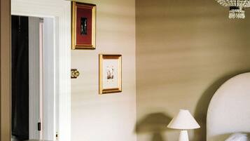 A room with a fireplace, a mirror reflecting a door and two framed pictures, and a chandelier.