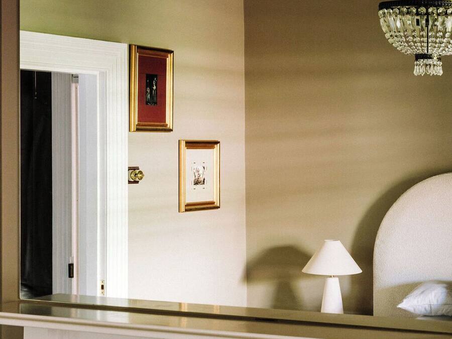 A room with a fireplace, a mirror reflecting a door and two framed pictures, and a chandelier.