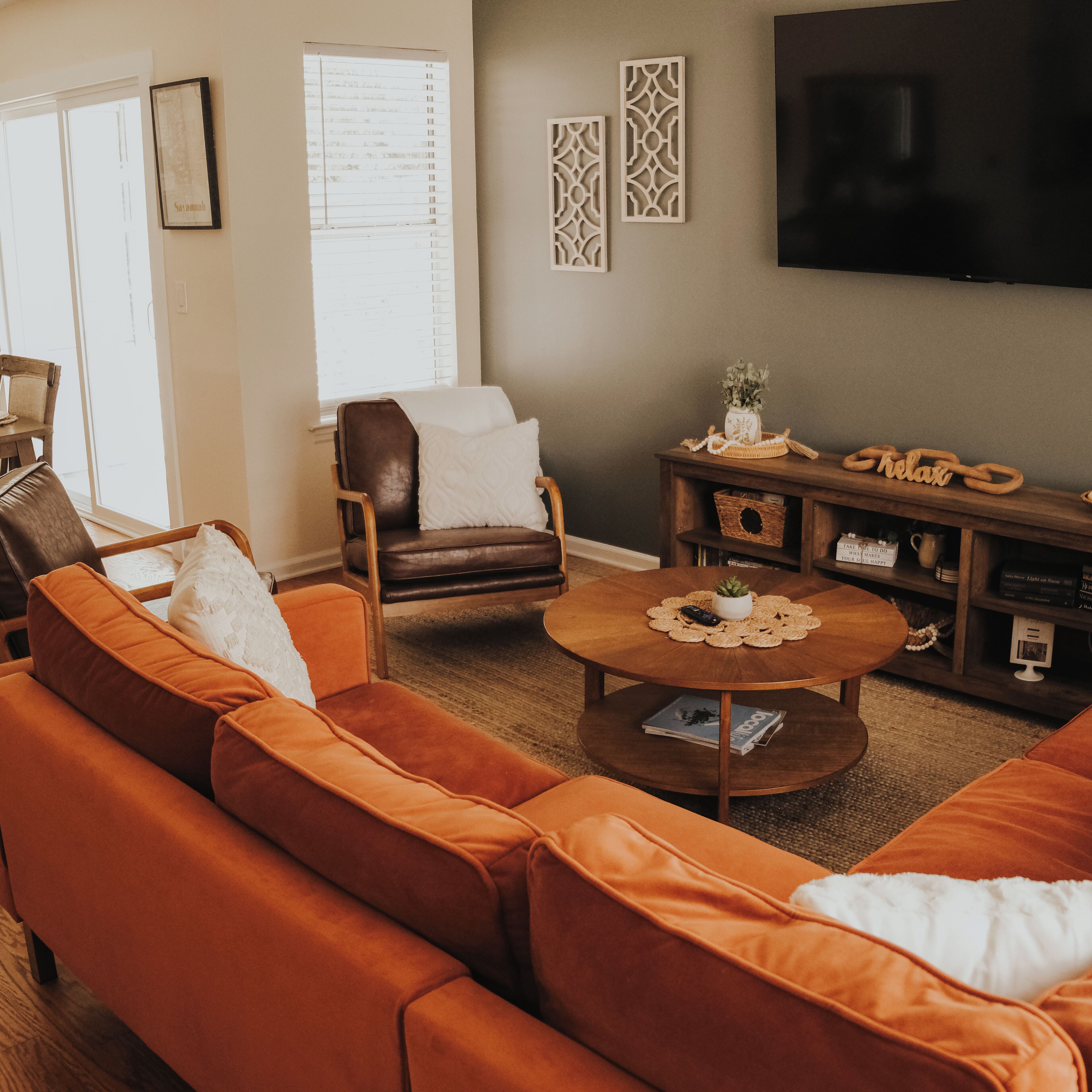 A living room with a brown leather sofa, a wooden coffee table, and a television mounted on the wall.